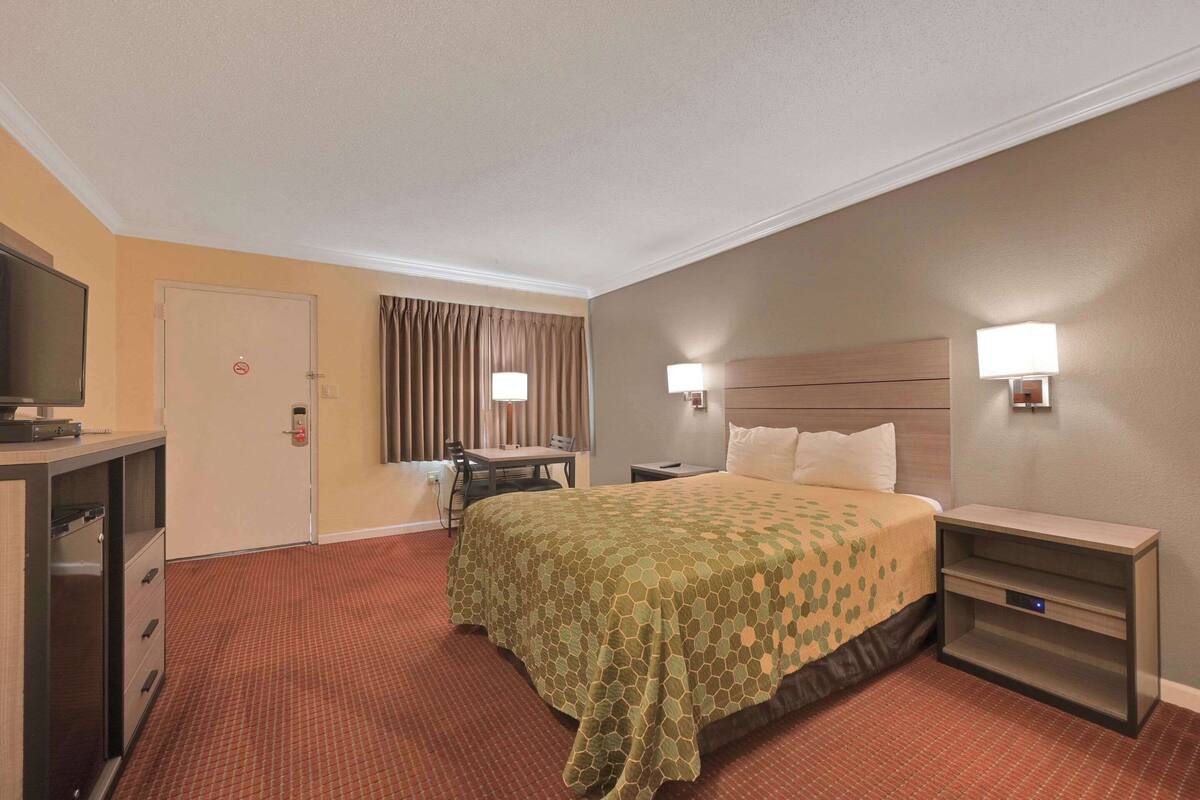 A hotel room with a bed, bedside tables, a desk, a chair, and a television.