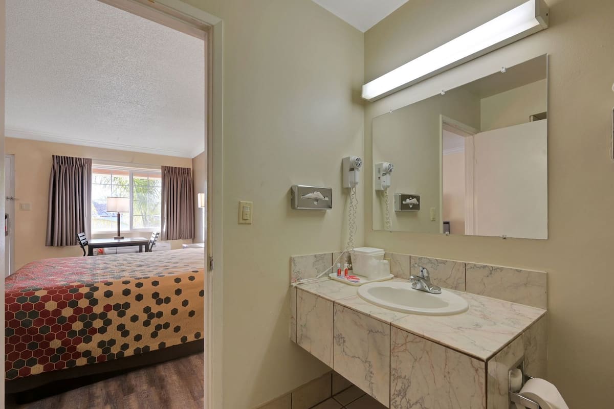 A hotel room with a bed, a bathroom with a sink and mirror, and a window with curtains.