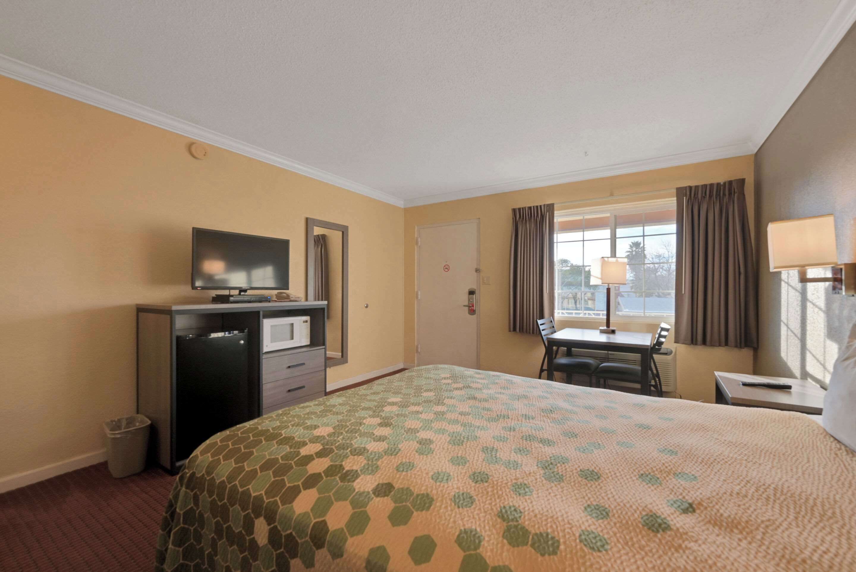 A hotel room with a bed, a desk, a television, and a window with curtains.