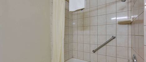 A bathroom with a bathtub, a shower, and a handrail.