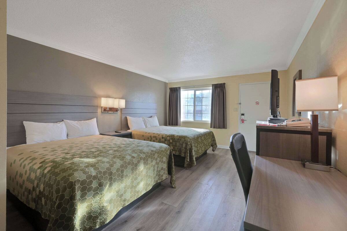 A hotel room with two beds, a desk, a chair, a TV, and a window with curtains.
