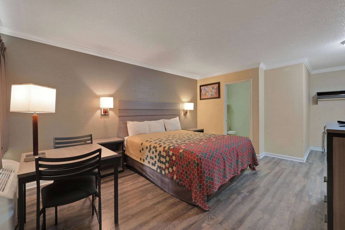 A hotel room with a bed, bedside table, lamp, chair, and a desk with a chair.