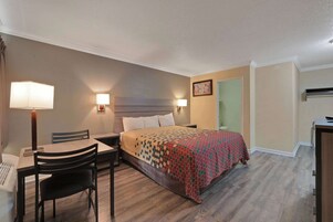 Una habitación de hotel con cama, mesita de noche, lámpara, silla y escritorio con otra silla.