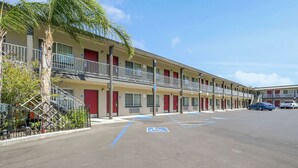 Un motel de dos pisos, un estacionamiento con espacios para discapacitados y una palmera en primer plano.