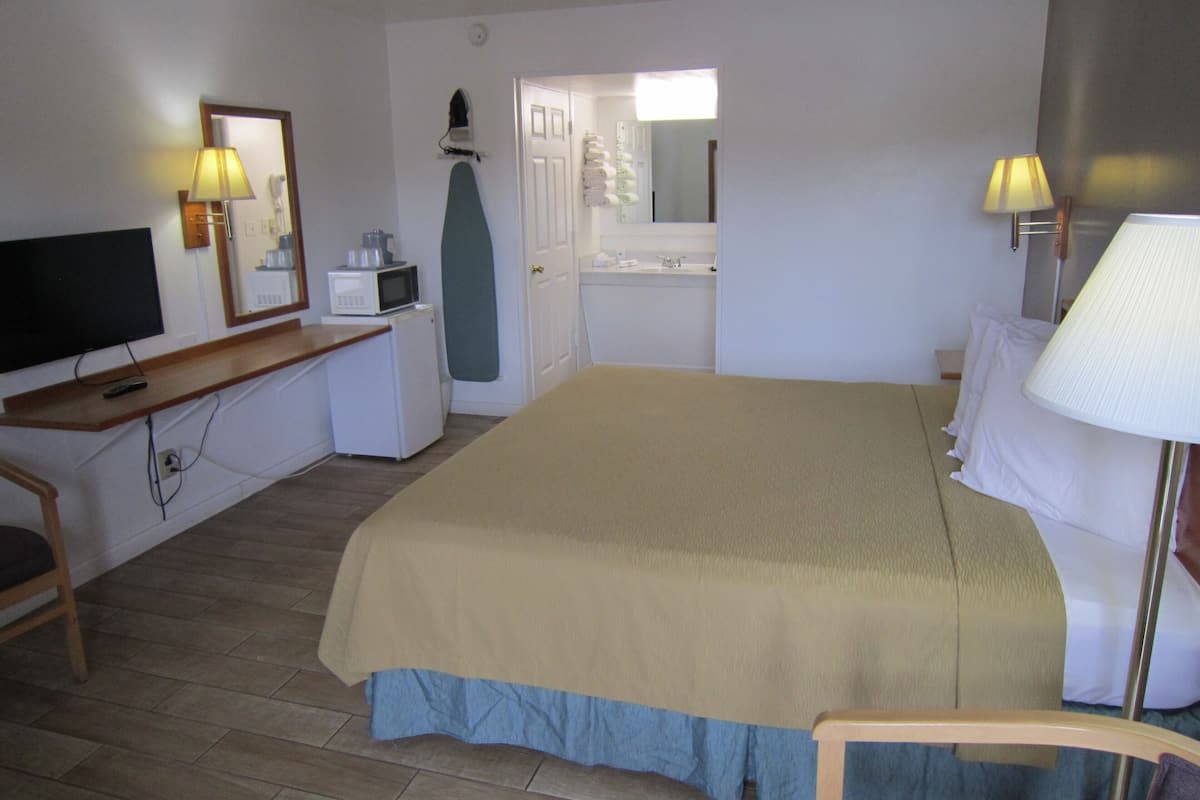 A hotel room with a bed, a desk with a TV, a microwave, and a small refrigerator.