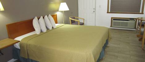A hotel room with a bed, a chair, a desk, a door, and a window.