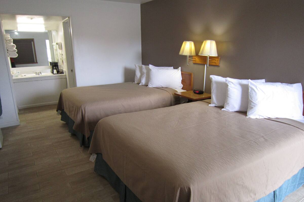 A hotel room with two beds, a nightstand with lamps, a mirror, and a bathroom visible through an open door.