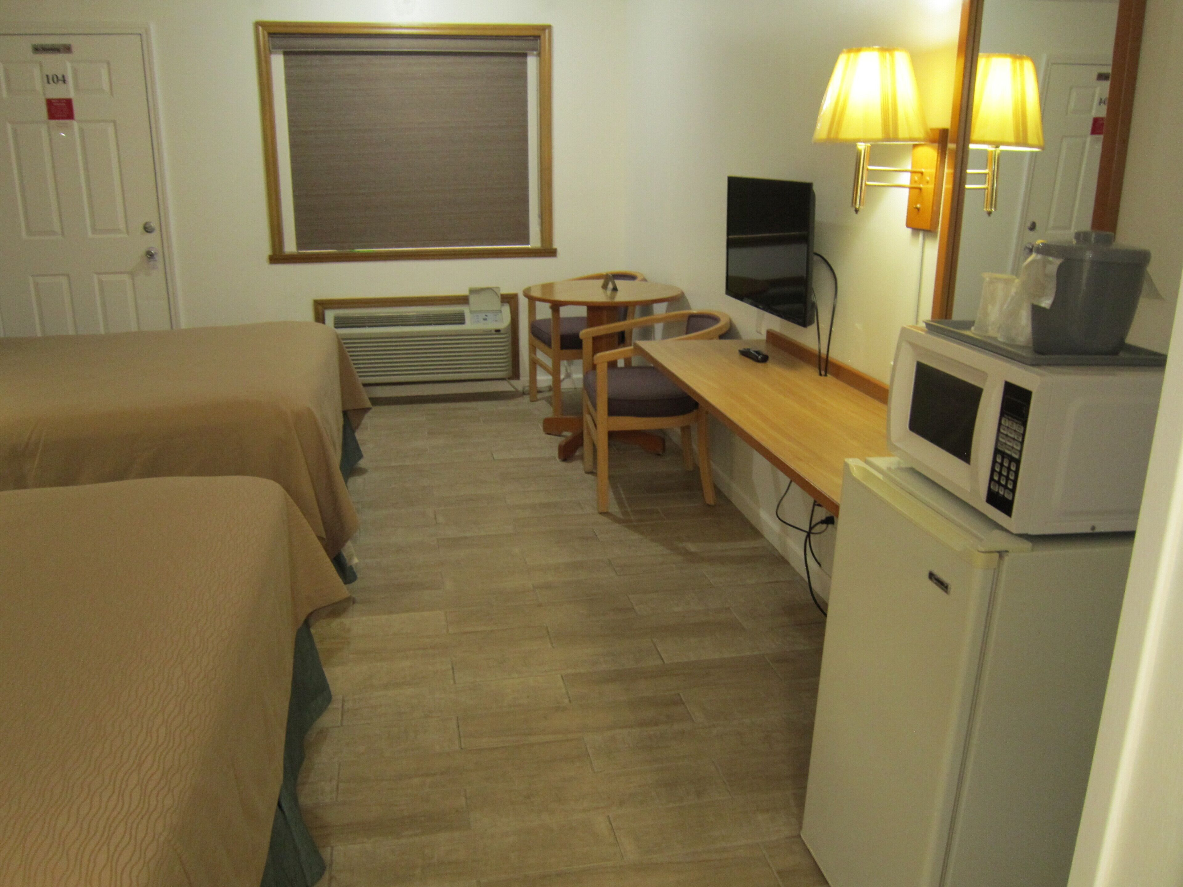 A hotel room with two beds, a desk, a chair, a TV, a microwave, and a heater.