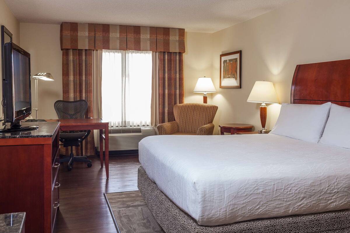 A hotel room with a bed, desk, chair, and two lamps.