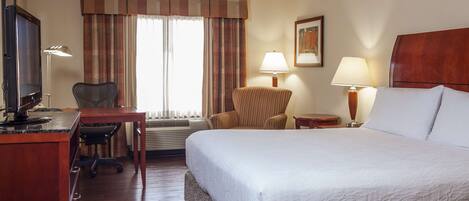 Una habitación de hotel con cama, escritorio, silla y dos lámparas.