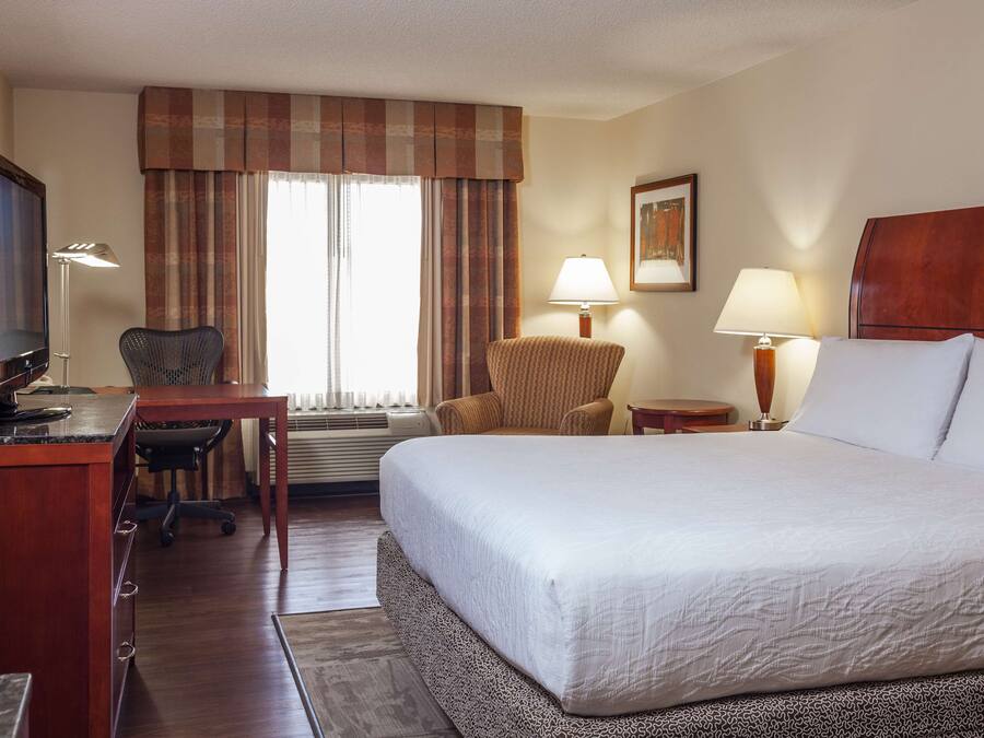 A hotel room with a bed, desk, chair, and two lamps.
