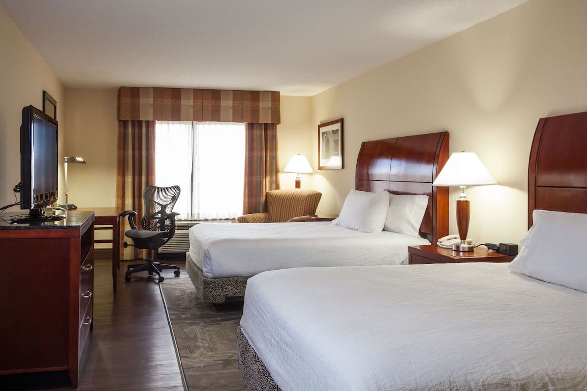 A hotel room with two beds, a desk with a computer, a chair, and a TV.