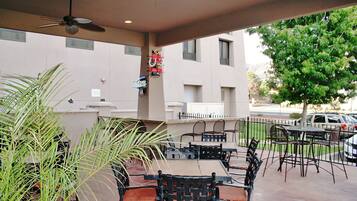 An outdoor patio area with tables and chairs, a ceiling fan, and a view of a building and parked cars.