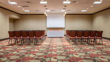 A conference room with a large screen at the front, rows of chairs on either side, and a patterned carpet.