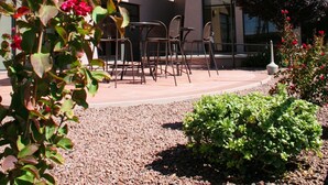 Exterior de un hotel con asientos al aire libre, un patio y un jardín con flores rojas.