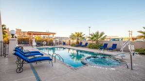 Un área de piscina con sillones de descanso, una bañera de hidromasaje y una pérgola.