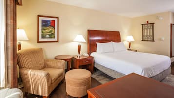 Une chambre d’hôtel avec un lit, une chaise, une table, une lampe, une table de chevet et un tableau au mur.