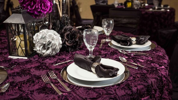 Mesa servida con platos, cubiertos y una servilleta doblada, adornada con elementos decorativos como flores y un farol.