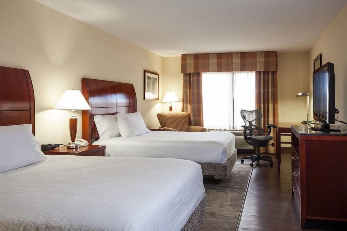 A hotel room with two beds, a desk with a computer, a chair, and a TV.