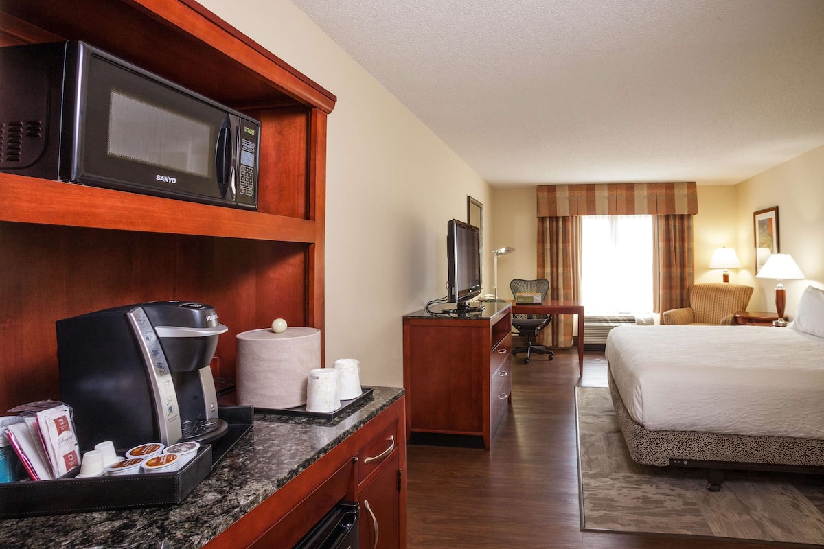 A hotel room with a kitchenette, a bed, a desk, and a TV.