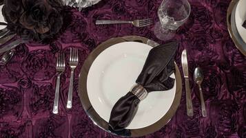 Una mesa dispuesta con un plato blanco, servilleta negra, cubiertos y una copa.