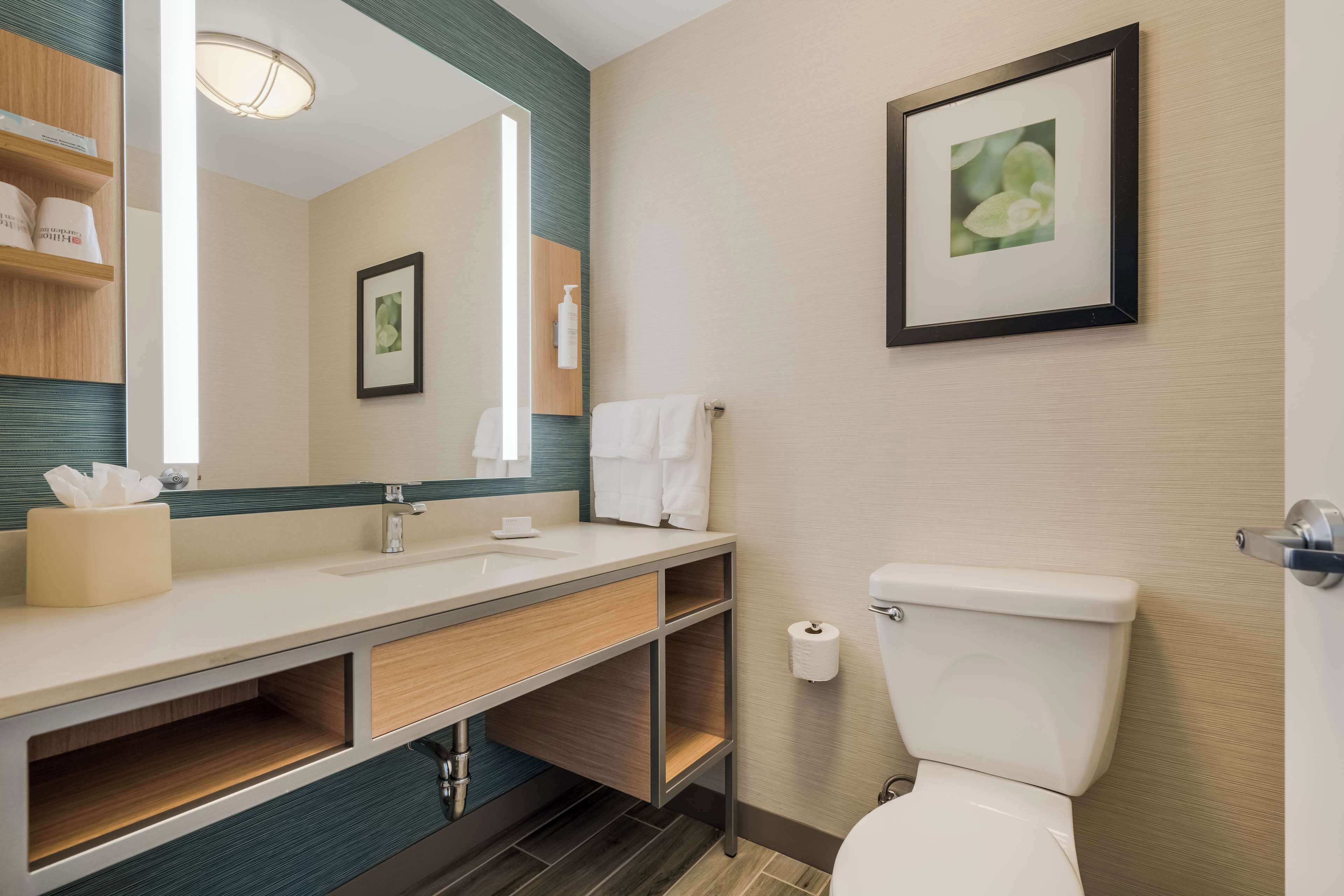 A modern bathroom with a large mirror, wooden vanity, white sink, and toilet.
