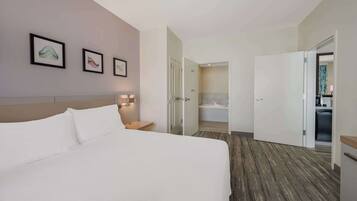Une chambre d’hôtel avec un grand lit, une table de chevet et des œuvres d’art accrochées au mur. On peut apercevoir la salle de bain à travers une porte ouverte.