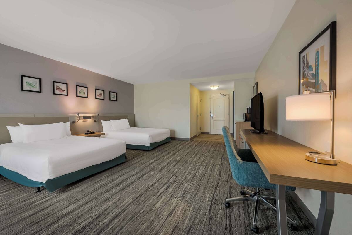 A hotel room with two beds, a desk with a chair, a television, and framed pictures on the wall.