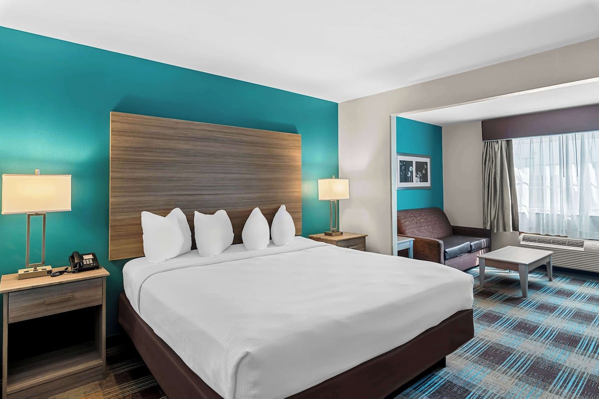 Une chambre d’hôtel avec un grand lit, deux tables de chevet avec des lampes, un bureau, une chaise et une grande fenêtre avec des rideaux.