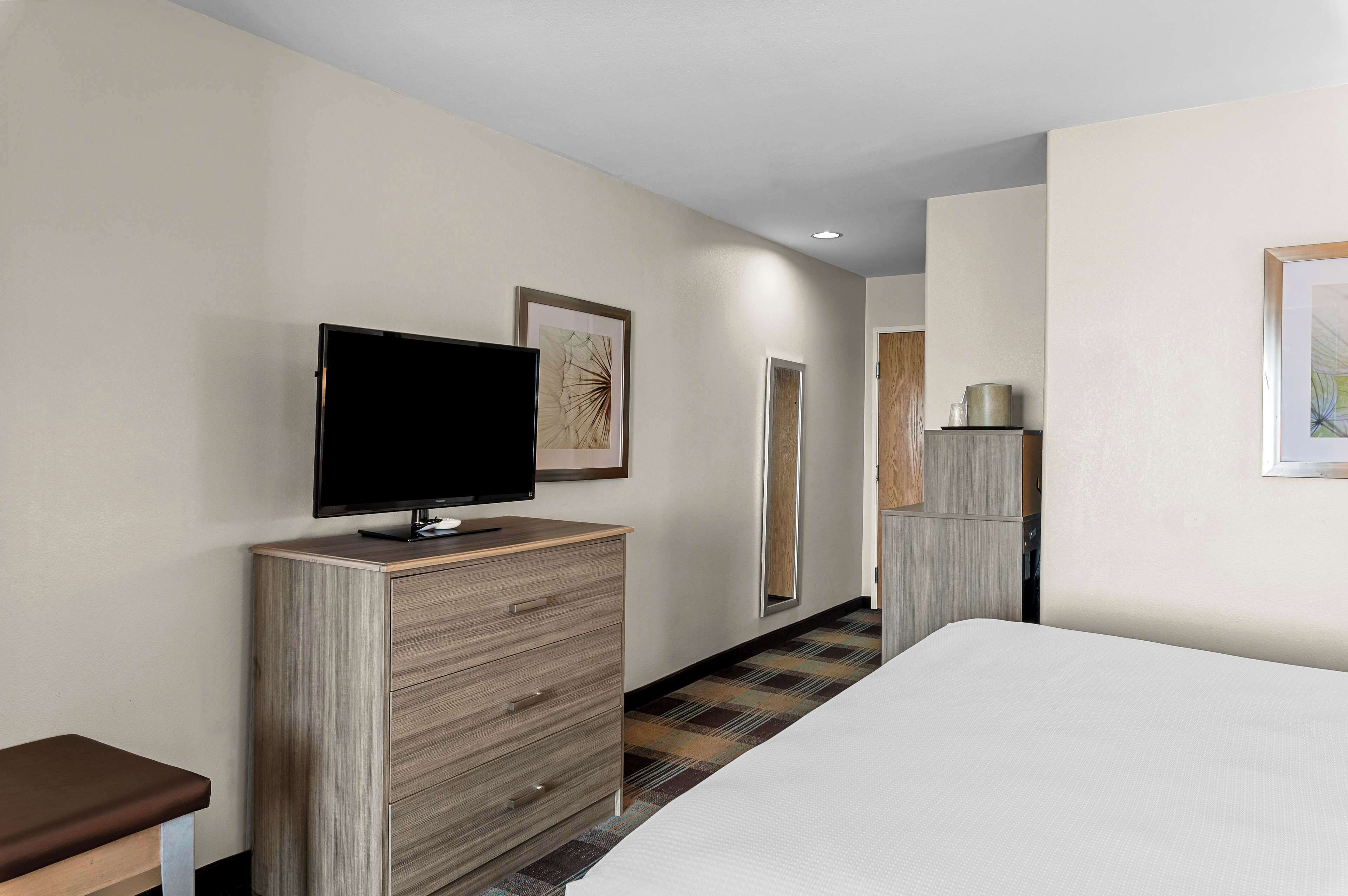 Habitación de hotel con una cama, un televisor sobre un tocador de madera, un banco y un espejo.