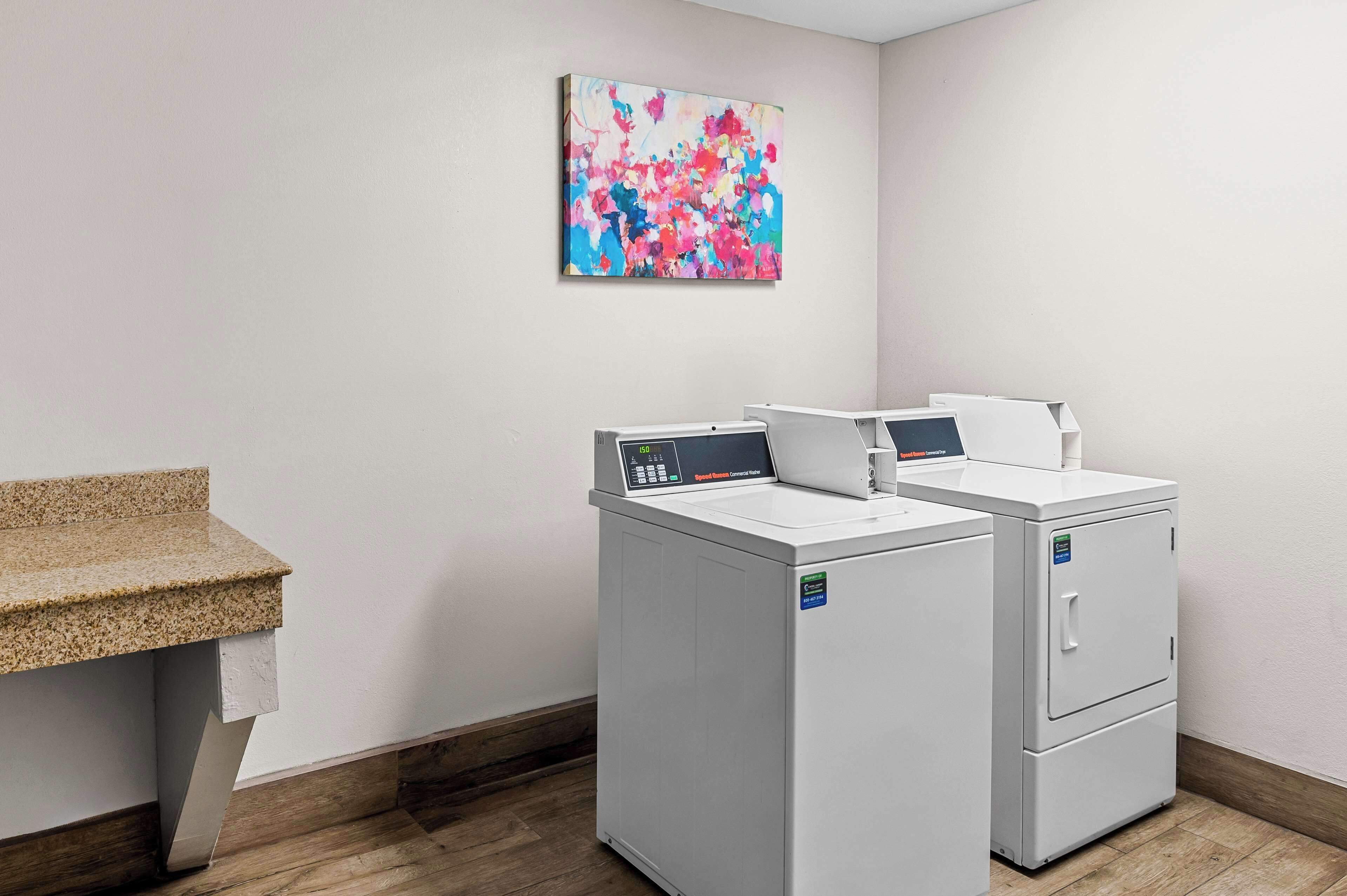 A laundry area with two front-loading washing machines, a bench, and a colorful abstract painting on the wall.