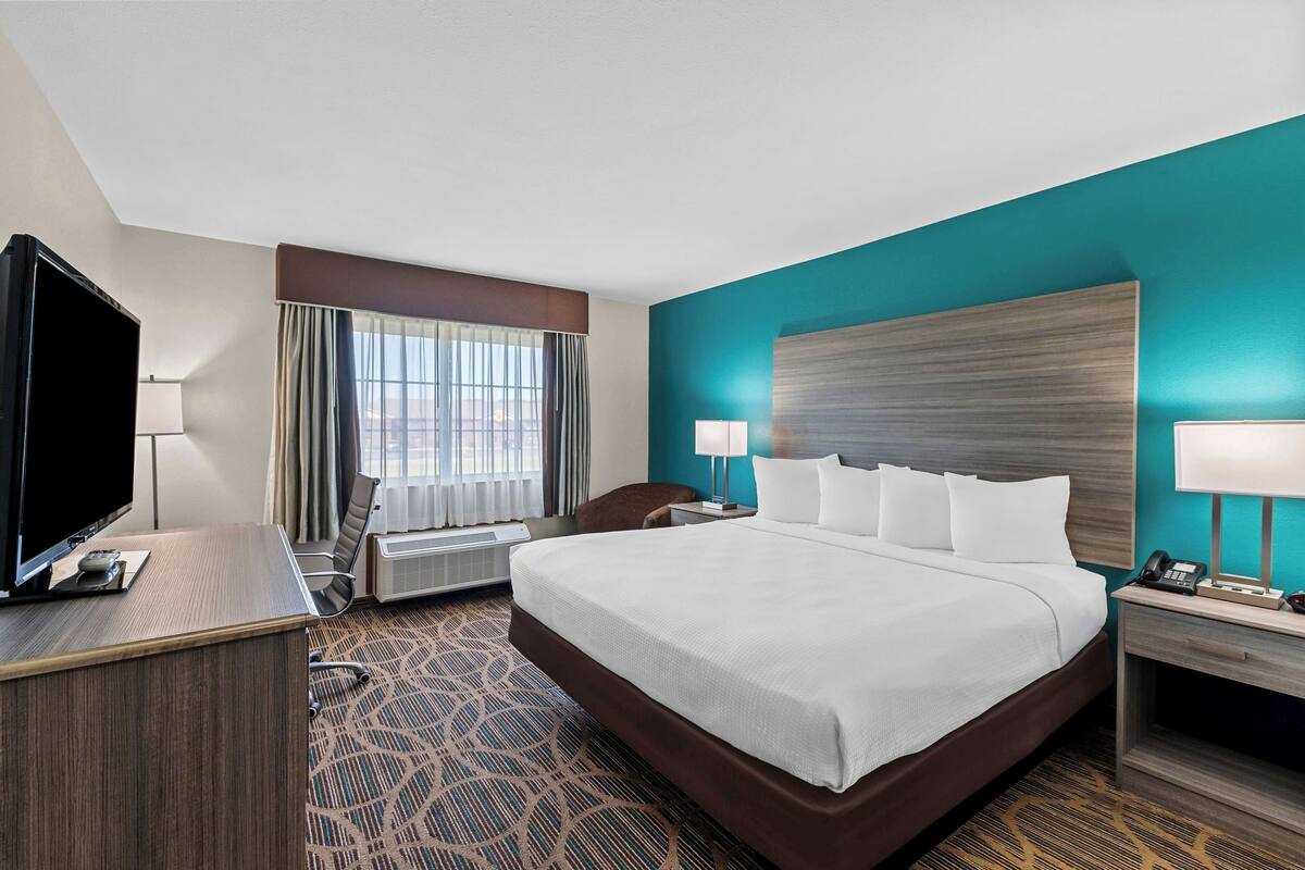 Une chambre d’hôtel avec un grand lit, un bureau doté d’un téléviseur à écran plat, une chaise, une fenêtre avec des rideaux et une vue sur la ville.
