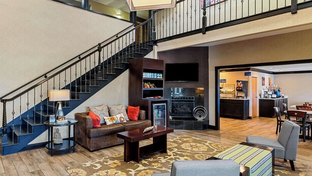 Un vaste espace de vie comprenant un escalier, un canapé avec des coussins, une machine à café et un coin repas avec des chaises.