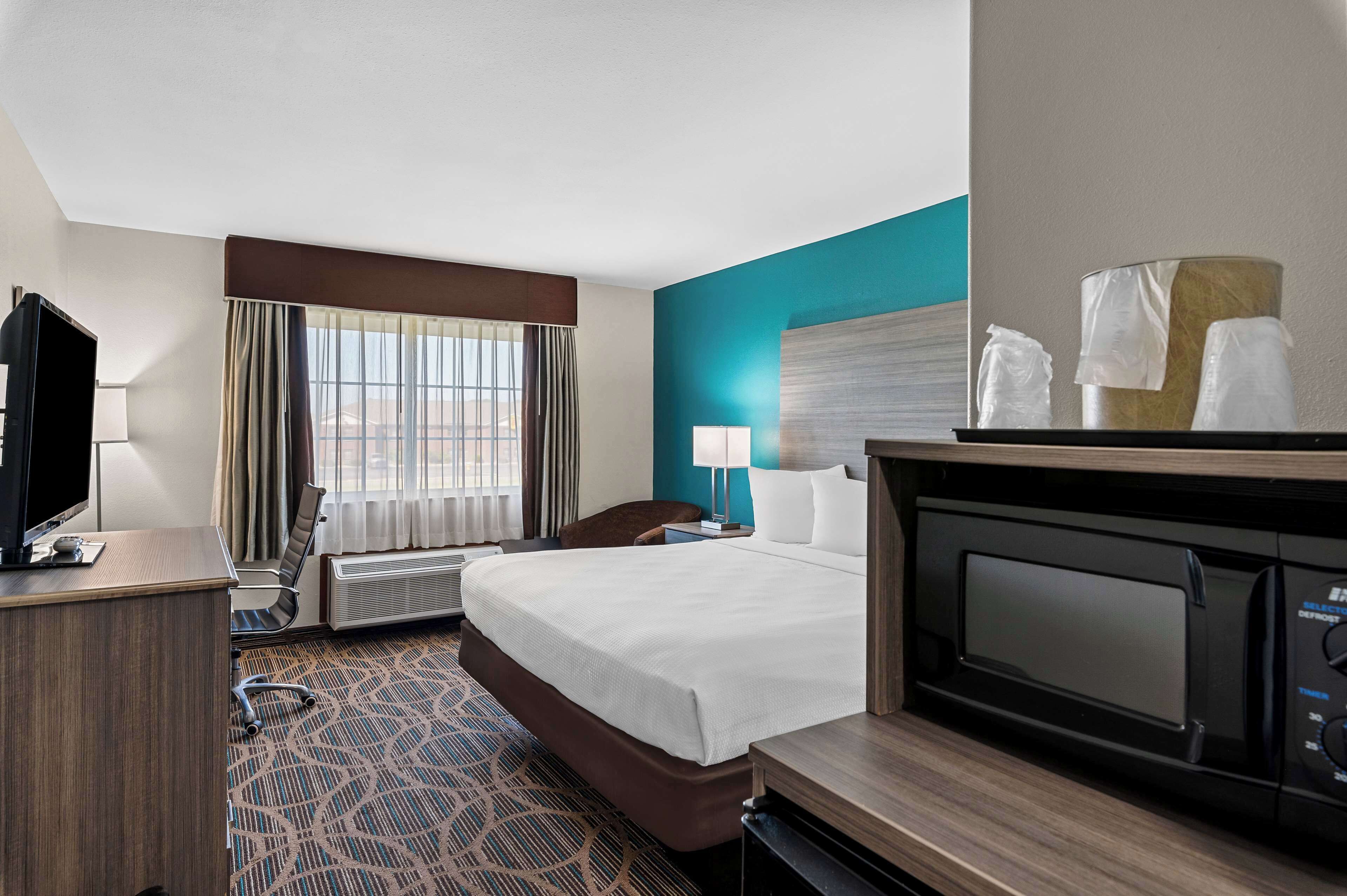 Ein Hotelzimmer mit Bett, Schreibtisch, Fernseher, Lampe, Stuhl und Mikrowelle.