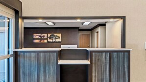 Un comptoir d’accueil avec un placage en bois foncé, un éclairage encastré et deux tableaux encadrés accrochés au mur.