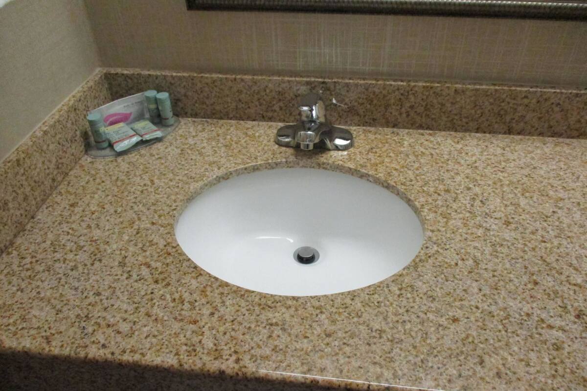Un lavabo de salle de bain avec un plan de toilette en granit, un robinet et un miroir au-dessus.