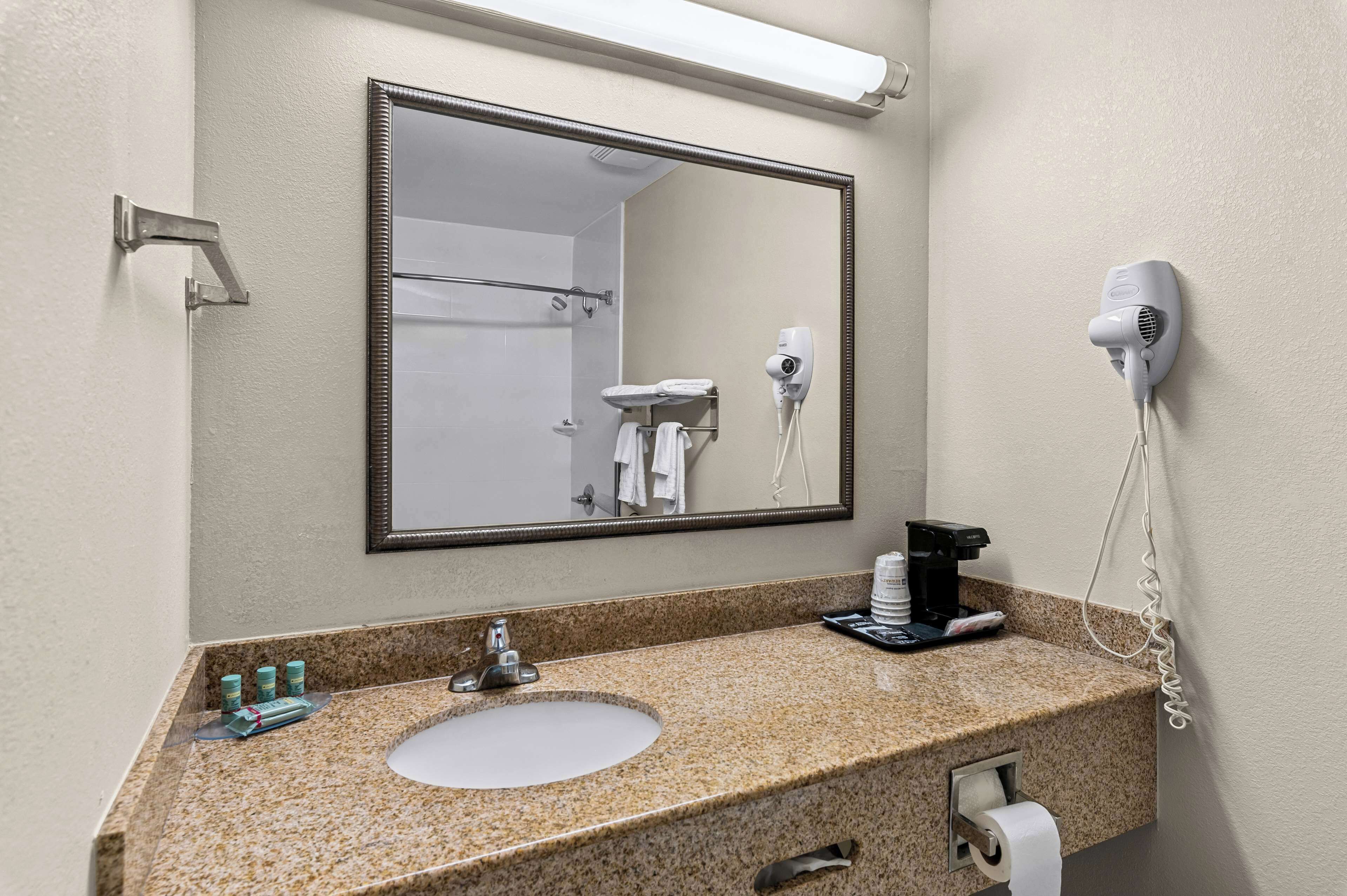 A bathroom with a granite countertop, a sink, a mirror, a hairdryer, and toiletries.