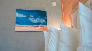 A room with a textured gray wall, a painting of a sunset over the ocean, and a white pillow.