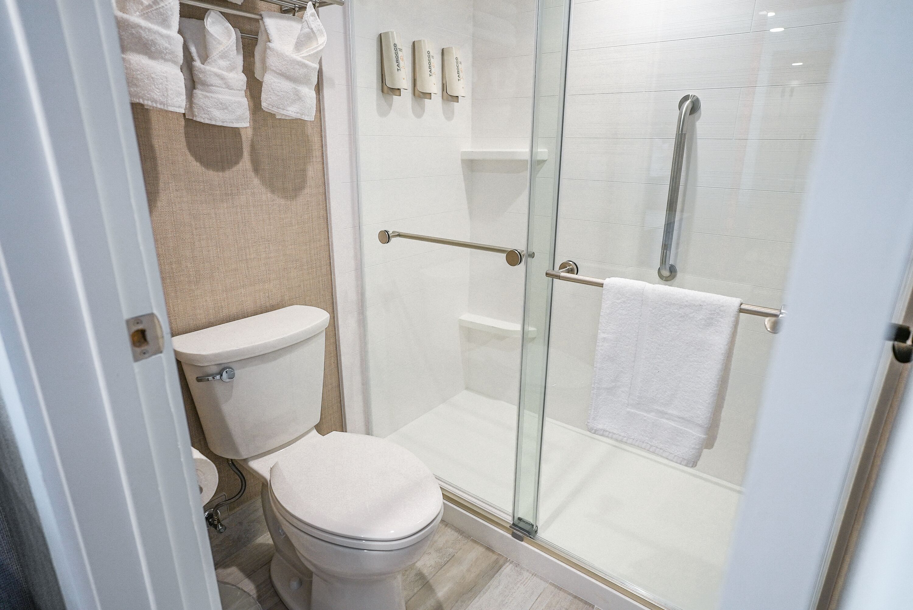 Een moderne badkamer met een toilet, een douchecabine en een handdoekrek met witte handdoeken.