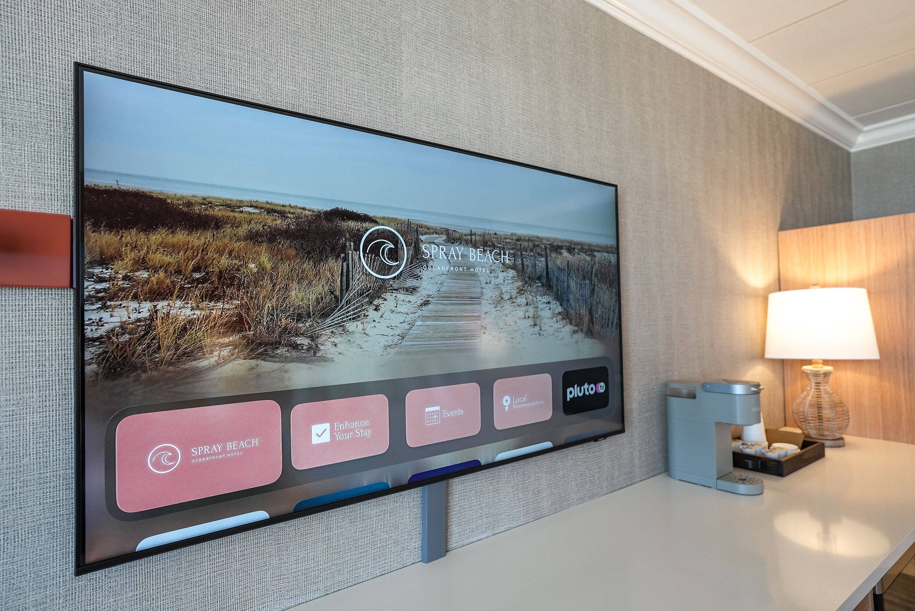 A television displaying a beach scene with a logo for Spray Beach Oceanfront Hotel.