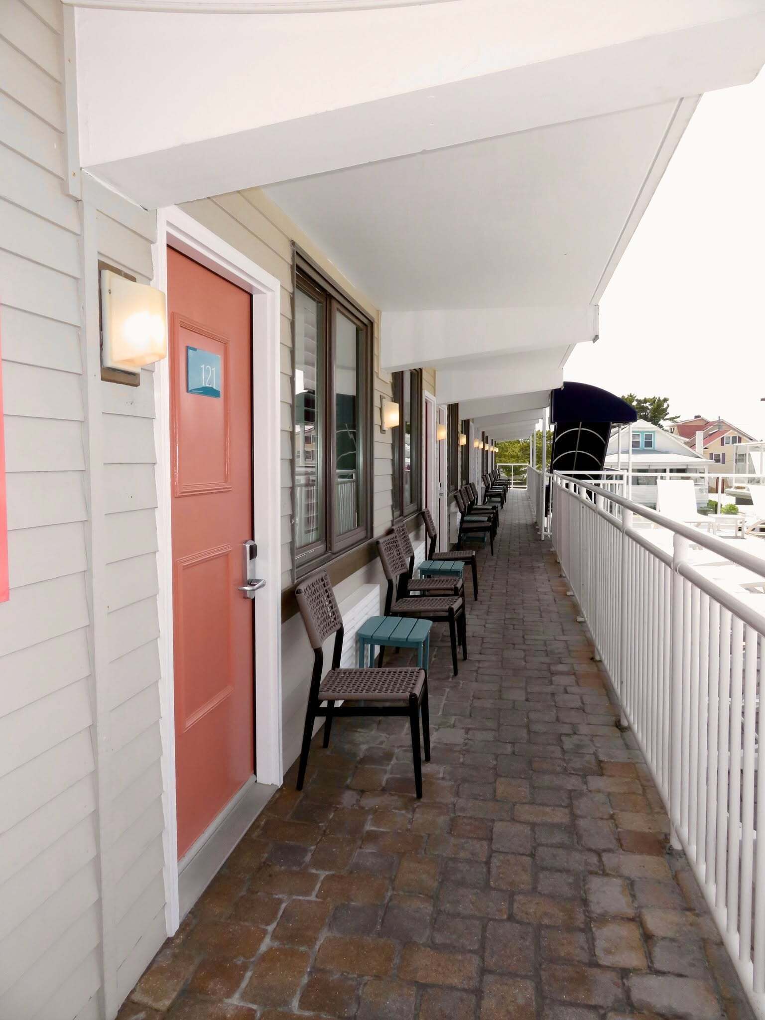 A covered outdoor seating area with chairs and tables, a red door, and a number sign indicating the room.