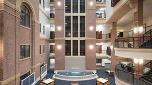 A spacious atrium with a central fountain, multiple floors with balconies, and a clock on the wall.