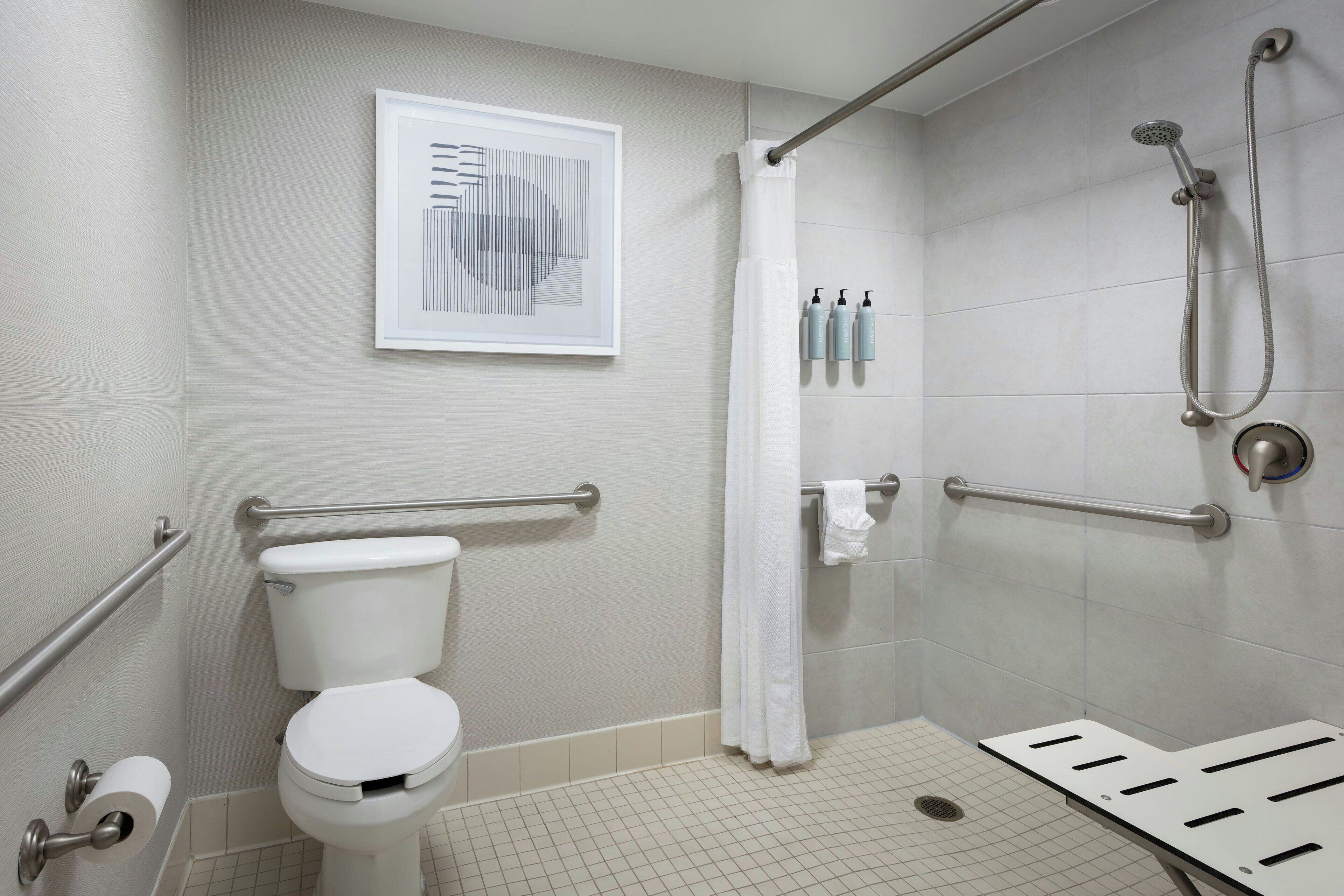 A bathroom with a toilet, a shower, and a handrail.