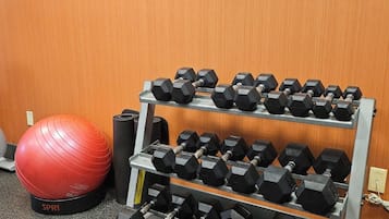 Un gimnasio con un estante de mancuernas, una pelota de ejercicios roja y un banco para pesas.