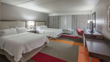 Una habitación de hotel con dos camas, un escritorio, una silla, un televisor y una ventana con cortinas.