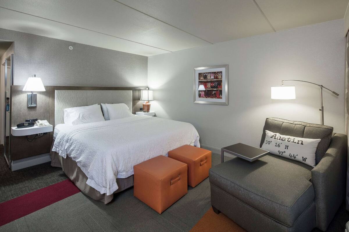 A hotel room with a bed, bedside lamps, a nightstand, a small table, a sofa, and a framed picture on the wall.