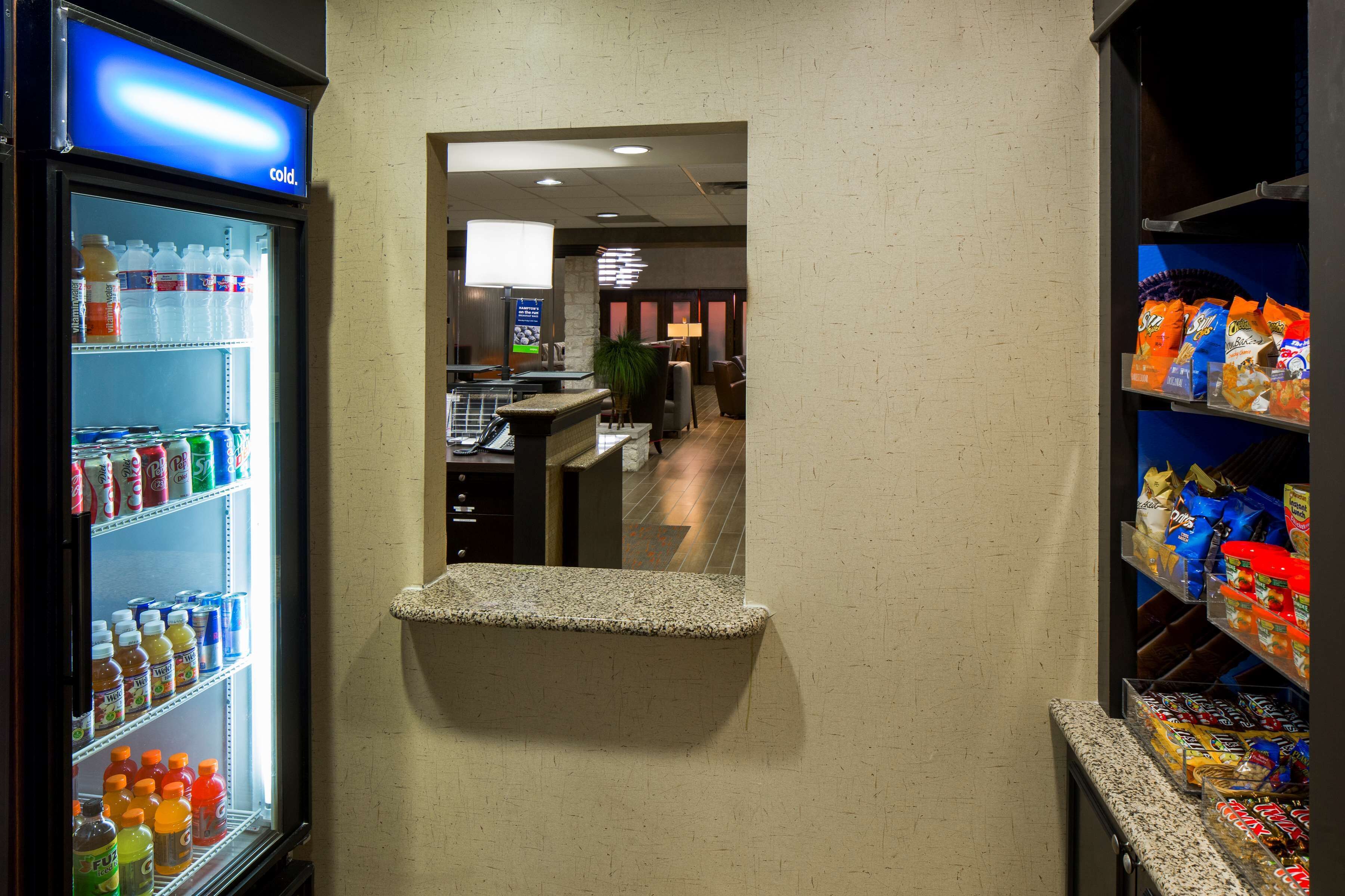 A hotel lobby with a refrigerator stocked with beverages, a seating area with a stone bench, and snack shelves.