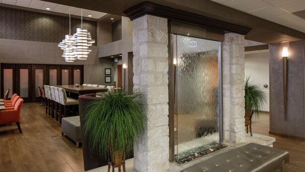 A modern lobby with a stone fireplace, a dining area with orange chairs, and a hanging light fixture. - Hampton Inn & Suites Austin Cedar Park-Lakeline (Austin)