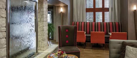 A lobby with a stone wall, a water feature, seating area with striped chairs, and a wooden table with magazines.