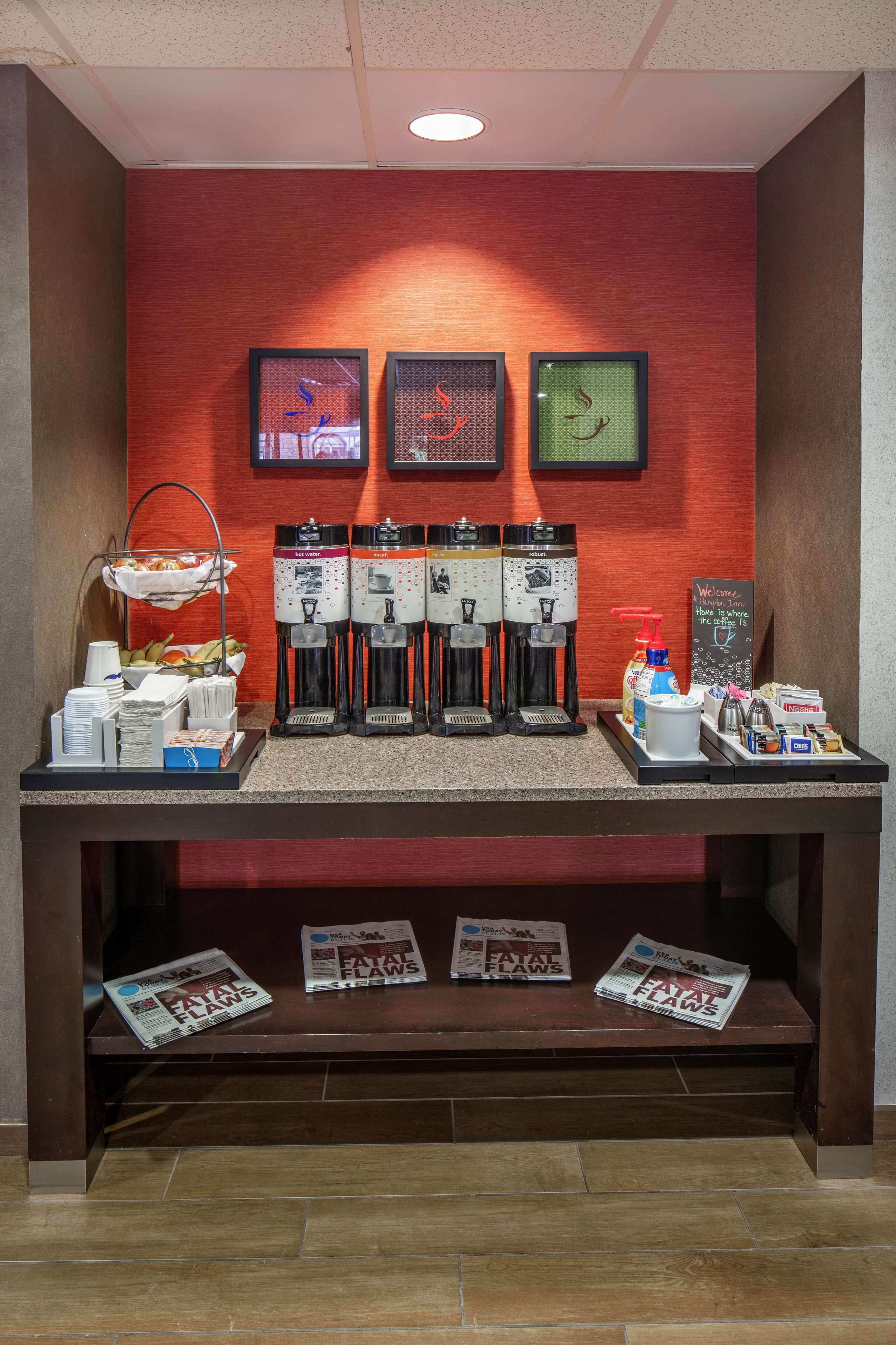 A coffee station with multiple coffee dispensers, a welcome sign, and newspapers on a wooden table.